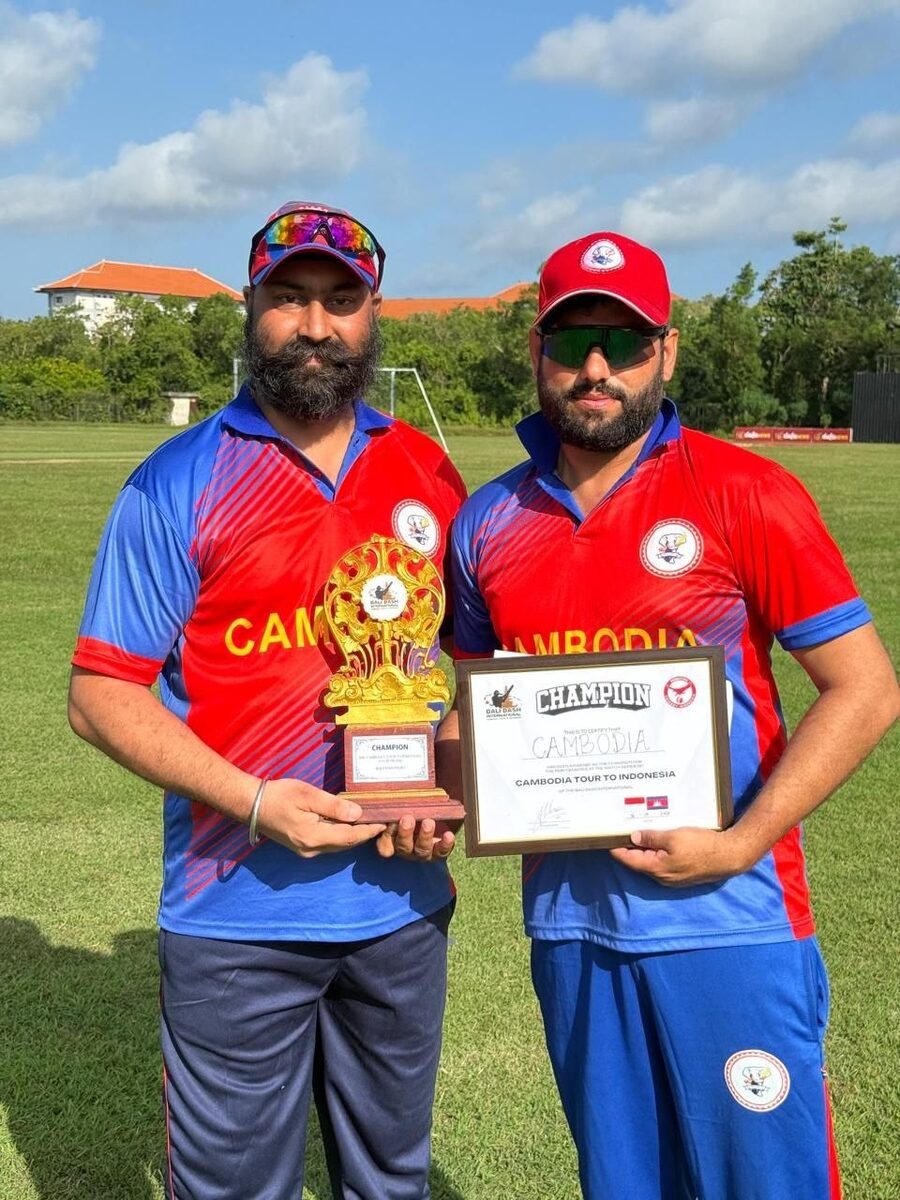 Two Cambodia players holding the Champion trophy and certificate